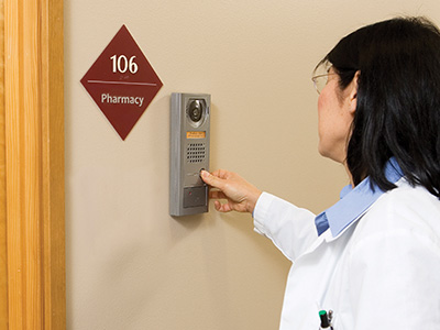 Doctor or nurse using an exchange-based video intercom door station with a built in prox point card reader to request entry into a secured pharmacy.