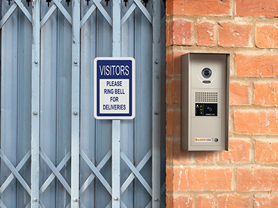 A hooded, weather resistant multi-tenant video entry station made from zinc die cast is mounted to the surface of a brick wall next to an accordion security gate to allow legitimate visitors a method to request entry into the building.