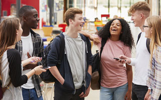 A ethnically and gender diverse group of students chat and laugh in the common area of their school